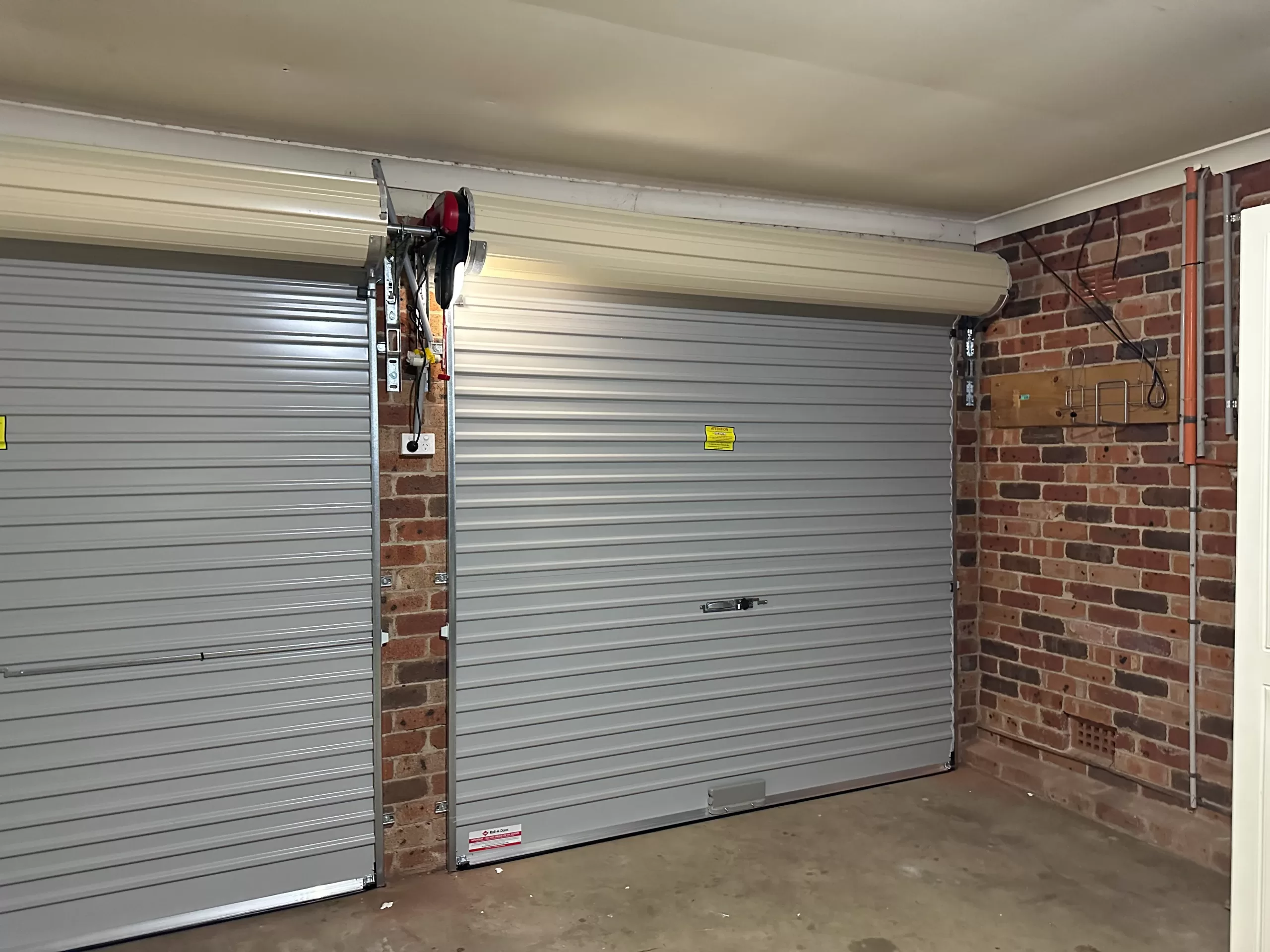 A closed gray roller garage door installed in a garage with exposed brick walls and an automated door opener mechanism on the side.