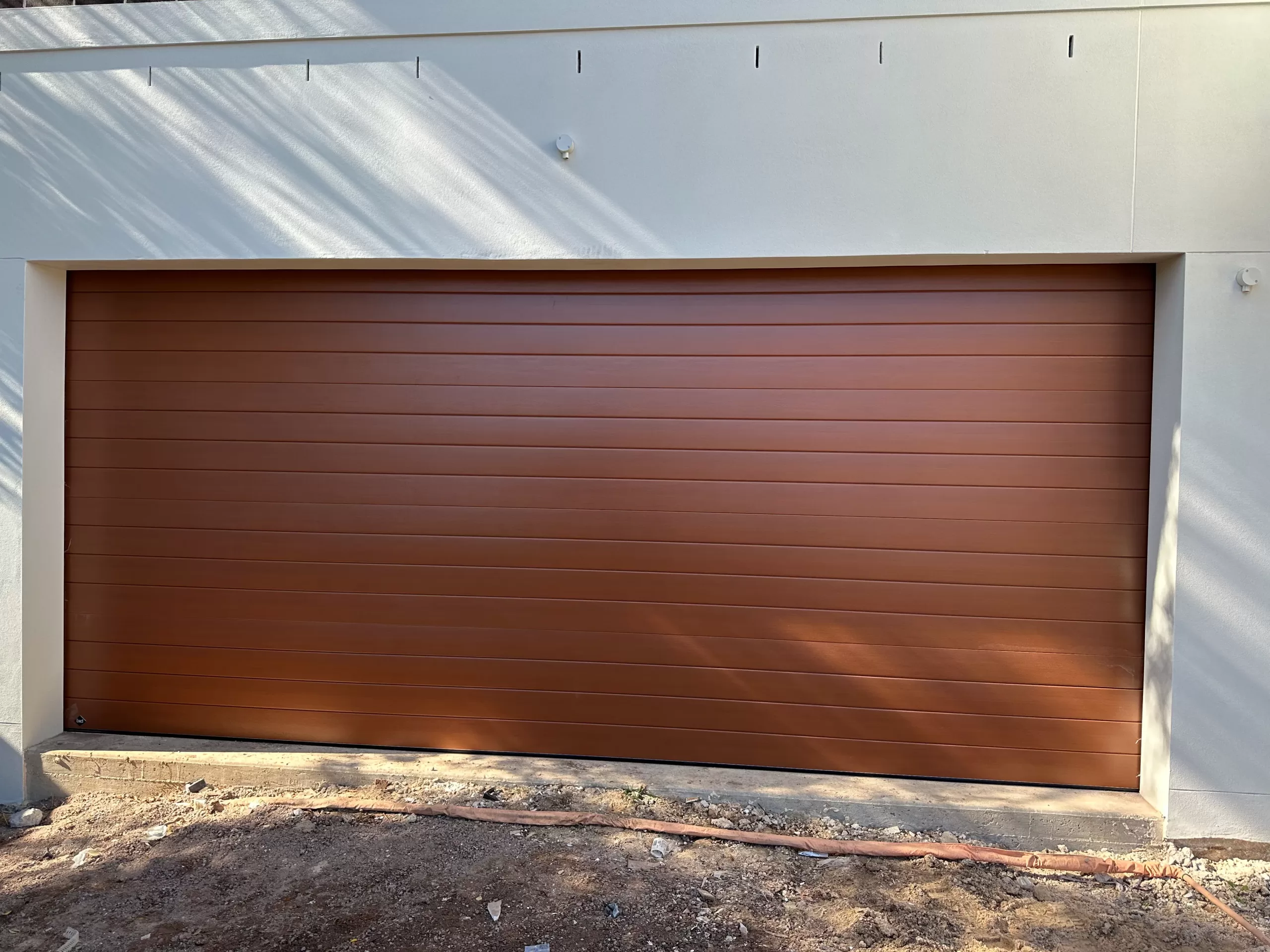 Brown tilt garage door closed with brick wall above.