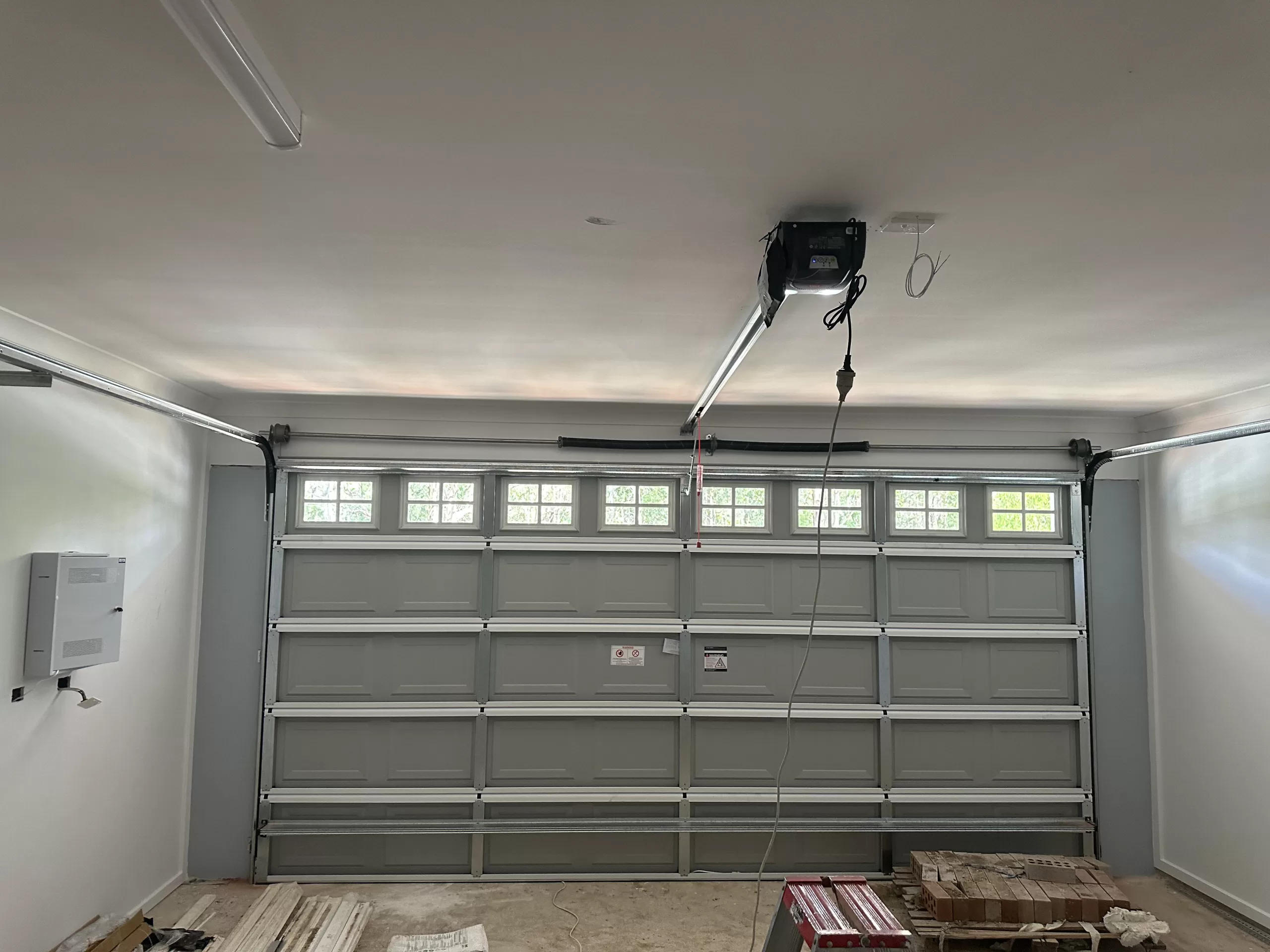 Interior view of a garage showing a partially open sectional door with windows and an automated opener system.